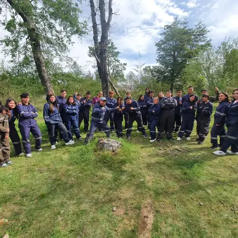 Curso con uniforme escolar posando en un prado rodeado de árboles